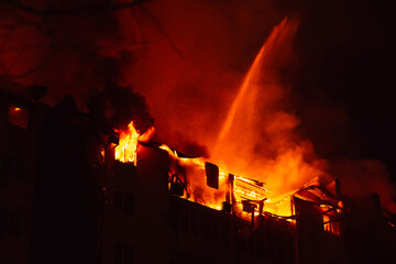 Dramatic night view of a building engulfed in flames with sparks flying, highlighting the intensity...