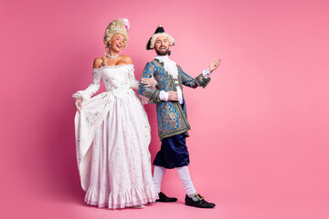 Fototapeta premium Elegant nobles in historic costumes posing against pink background at a themed event
