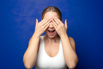 blonde woman smiling and feeling happy, covering eyes with both hands and waiting for unbelievable...