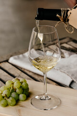 Pouring white wine into glass on a rustic table with a bunch of green grapes
