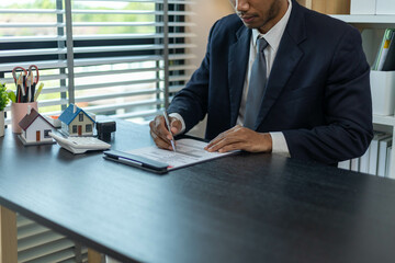 A man is sitting at a desk with a calculator and a piece of paper with numbers on it. He is...