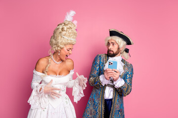Elegant Couple Dressed in Historic Costumes Interacting in Front of a Pink Background
