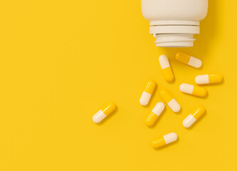 Yellow and white capsules spilled from white plastic bottle on yellow background. Top view with space for text.