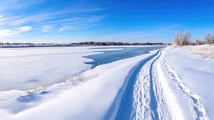 Snowy landscape with tracks leading to frozen lake under clear blue sky