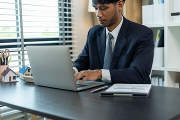 A man in a suit is typing on a laptop at a desk. Concept of professionalism and focus, as the man is dressed in a business suit and he is working on important tasks. The presence of the laptop
