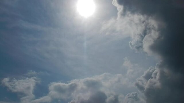 Blue sunny sky with sun, white Cirrus clouds and stormy dark clouds slowly moving - natural sky background with different types of clouds at different heights. Topics: weather change, cloudscape