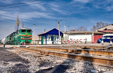 A green locomotive pulls tank cars against a blue sky.