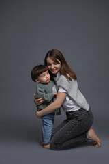 Happy mother hugging her little son on grey background