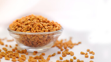 A bowl of Organic Fenugreek seeds (Trigonella foenum-graecum) powder, placed over a heap of whole fenugreek seeds. Isolated on a white background.