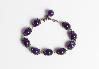 A bracelet of smooth round natural amethyst beads with silver clasp, on white background.