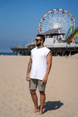 Man wearing glasses young tourist strolling along the beach by the pier in Santa Monica, California.