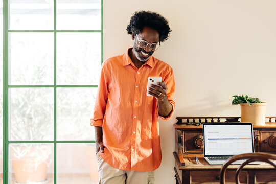 Mature black man smiling and reading a text message on smartphone at home