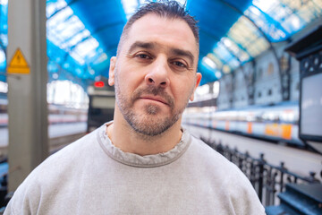  Close-up of a middle-aged man in a gray sweatshirt gazing upward at a train station. His...
