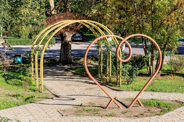 Heart-shaped sculpture in a park with archway and lush greenery