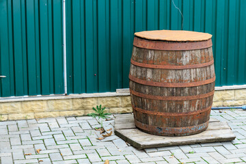 Rustic wooden barrel against green metal wall on stone pavement