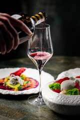 A hand pours red wine into a glass, accentuating a gourmet dining experience. Stylish plates feature vibrant dishes, enhancing the elegance of the setting. Perfect for food and beverage themes.