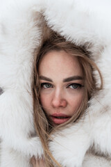 a close-up portrait of a blonde wrapped in a white fur coat