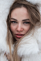 a close-up portrait of a blonde wrapped in a white fur coat
