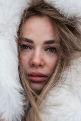 a close-up portrait of a blonde wrapped in a white fur coat