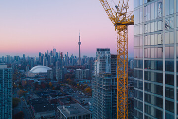 yellow crawler crane positioning glazed curtain wall panel, urban construction site