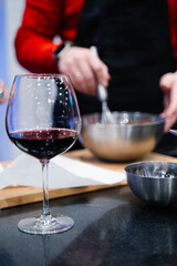 a glass of red wine against the background of a figure of a person preparing food