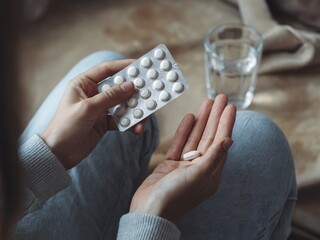 Person Holding Medication Pills With Glass of Water Nearby
