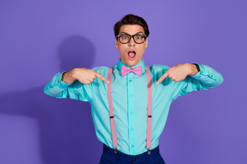 Stylish young man in retro outfit pointing at himself with a surprised expression against a vibrant purple background