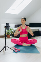 A woman in a pink sports suit conducting an online workout session via her smartphone