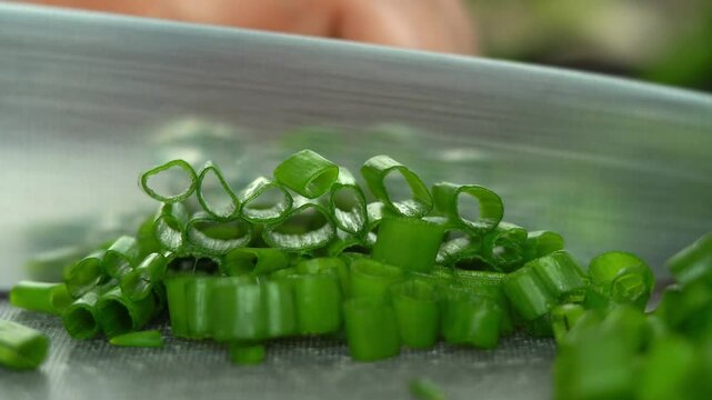Close up of chefs hands cut fresh green onions on cutting board with kitchen knife. Greens vegetables. Cooking food