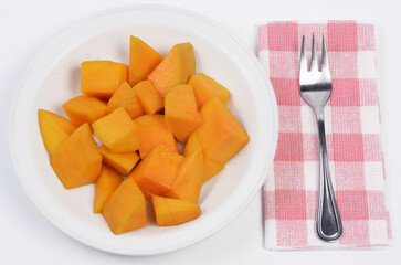 Cut mango fruit on a white plate and a small fork on a napkin.