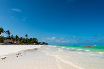 Plage ensoleillée de Zanzibar, eau turquoise, bateaux amarrés, palmiers soumis aux vents du large
