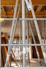 New building, with a scaffold on the outside. Inside many metal columns stailizing the freshly concreted ceiling construction.Selective focus, vertical photograph.