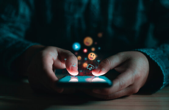 Close-up of hands using a smartphone in a dark setting, with floating social media icons representing engagement, communication, and digital interaction.