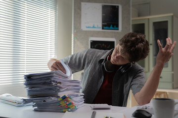 Young office worker struggling with a large stack of documents, wearing headphones, appearing...