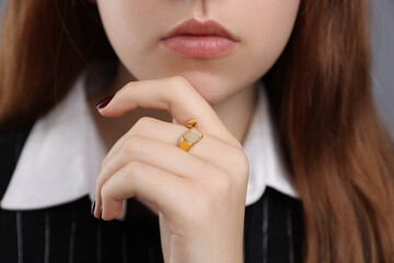 Teenage girl wearing stylish ring on grey background, closeup
