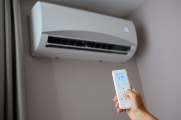 Man's hand holds air conditioner remote control and sets cooling temperature on split system to 17 degrees. Concept of air cooling in heat of room, climate control at home.