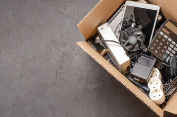 Old electronic devices in a cardboard box. The concept of recycling used gadgets. Black background
