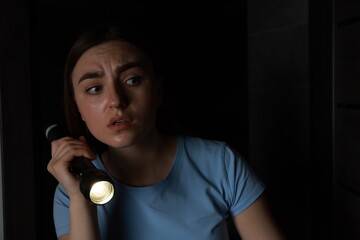 Fear of darkness. Scared young woman with flashlight indoors at night
