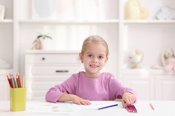 Happy girl at white table with drawing and pencils in kindergarten