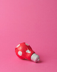 Light bulb in red gift wrapping with white polka dots on a pink background. Concept of...