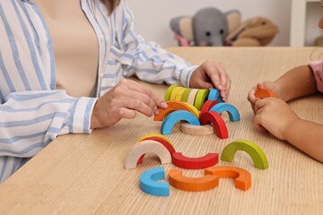 Autism therapy. Psychologist and little girl playing with educational toy at wooden table, closeup