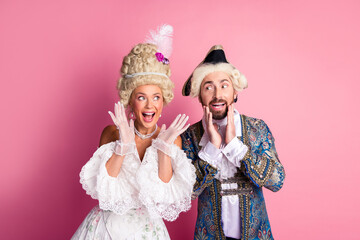 Elegant couple in historical clothing enjoying a playful moment with a pink background