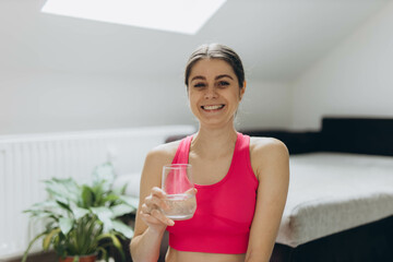 A sporty woman in a pink outfit holds a glass of water, representing health and fitness