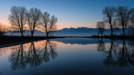 Fototapeta premium A calm lake reflecting the horizontal silhouette of trees and mountains in the serene twilight hour