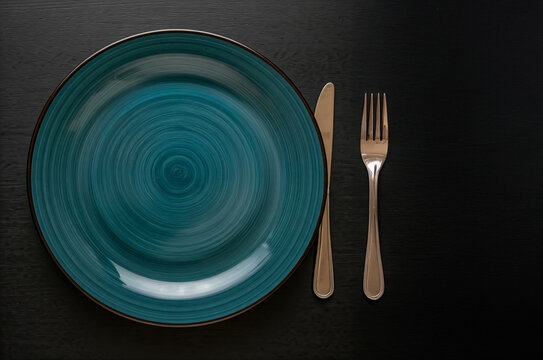 Table setting with empty plate and cutlery on black stone background.