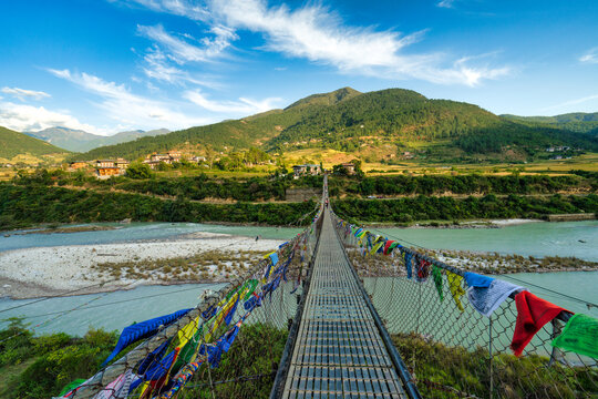 People crossing the pedestrian suspension Bridge decorated with prayer flags over the Po Chhu River, Punakha, Bhutan