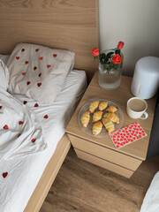 Romantic bedroom interior heart patterned white linens, croissants, roses, and steaming tea, valentine's day morning