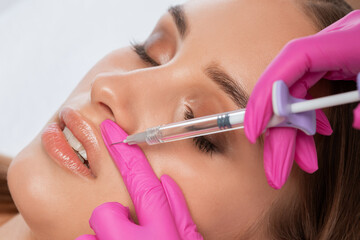 Cosmetologist does injections for lips augmentation and anti wrinkle in the nasolabial folds of a...