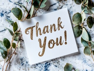 Naklejka premium Elegant thank you card with gold-foil lettering surrounded by eucalyptus leaves on marble surface