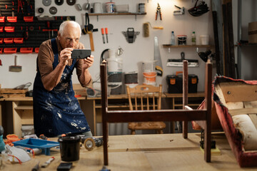 Senor carpenter restorer of old wooden furniture taking photo of old chair working in his workshop...